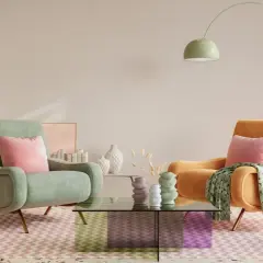Mięta i pomarańczowy fotel, różowe poduszki i dywanik w zygzaki tworzą przytulną atmosferę. Całość w **ciepłe pastelowe kolory**.