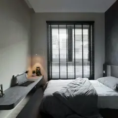 Nowoczesna, szara sypialnia z minimalistycznym biurkiem, laptopem i wygodnym łóżkiem.