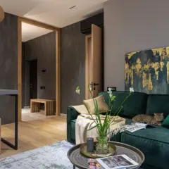 Elegancki salon z butelkowozieloną kanapą, na której leży kot. Złoto-granatowy obraz i jasne dodatki pokazują, jaki kolor pasuje do zielonego butelkowego.