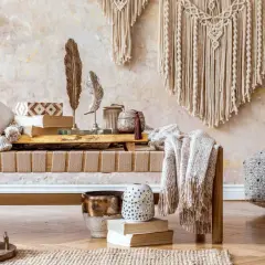 Przytulny pokój w stylu boho z makramą na ścianie, ławką z poduszkami i kocem, ozdobami z piór i wazonami.