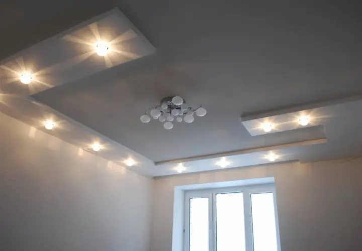 Nowoczesny sufit z wieloma punktami świetlnymi, tworzącymi rozproszone światło. Centralnie umieszczony designerski żyrandol.
