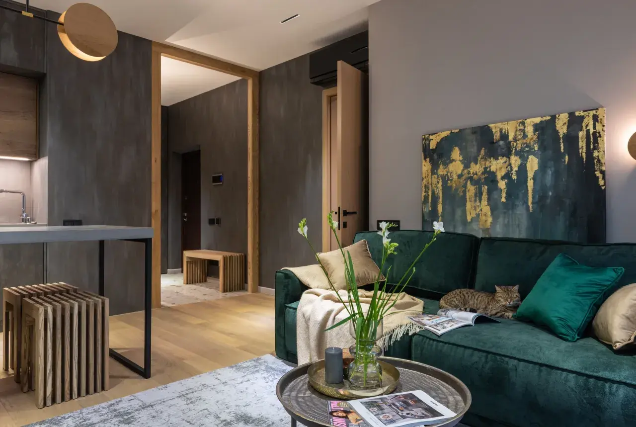Elegancki salon z butelkowozieloną kanapą, na której leży kot. Złoto-granatowy obraz i jasne dodatki pokazują, jaki kolor pasuje do zielonego butelkowego.