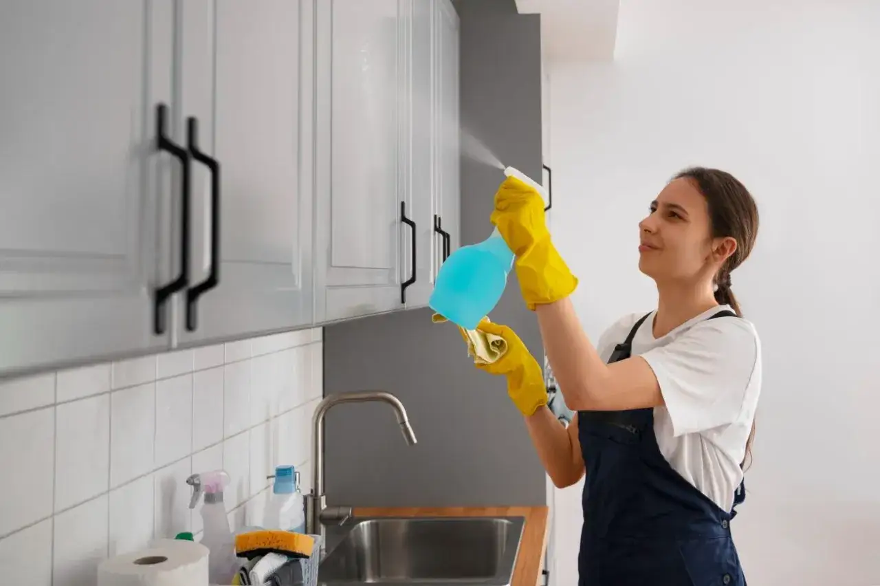 Kobieta w żółtych rękawiczkach czyści meble kuchenne z okleiny, używając sprayu i ściereczki.