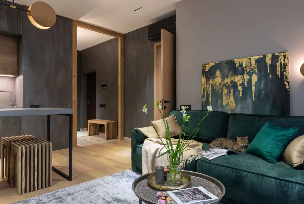 Elegancki salon z butelkową zieloną kanapą, na której leży kot. Złote akcenty na obrazie i poduszce pokazują, jaki kolor pasuje do zielonego butelkowego.