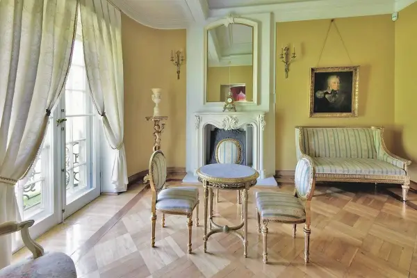 Elegancki salon w stylu pałacowym z kanapą, dwoma krzesłami, stolikiem i kominkiem.